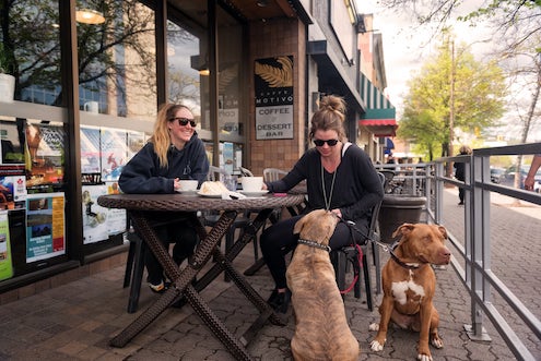 Two women having coffee outdoors with dogs at side at coffee shop in Kamloops